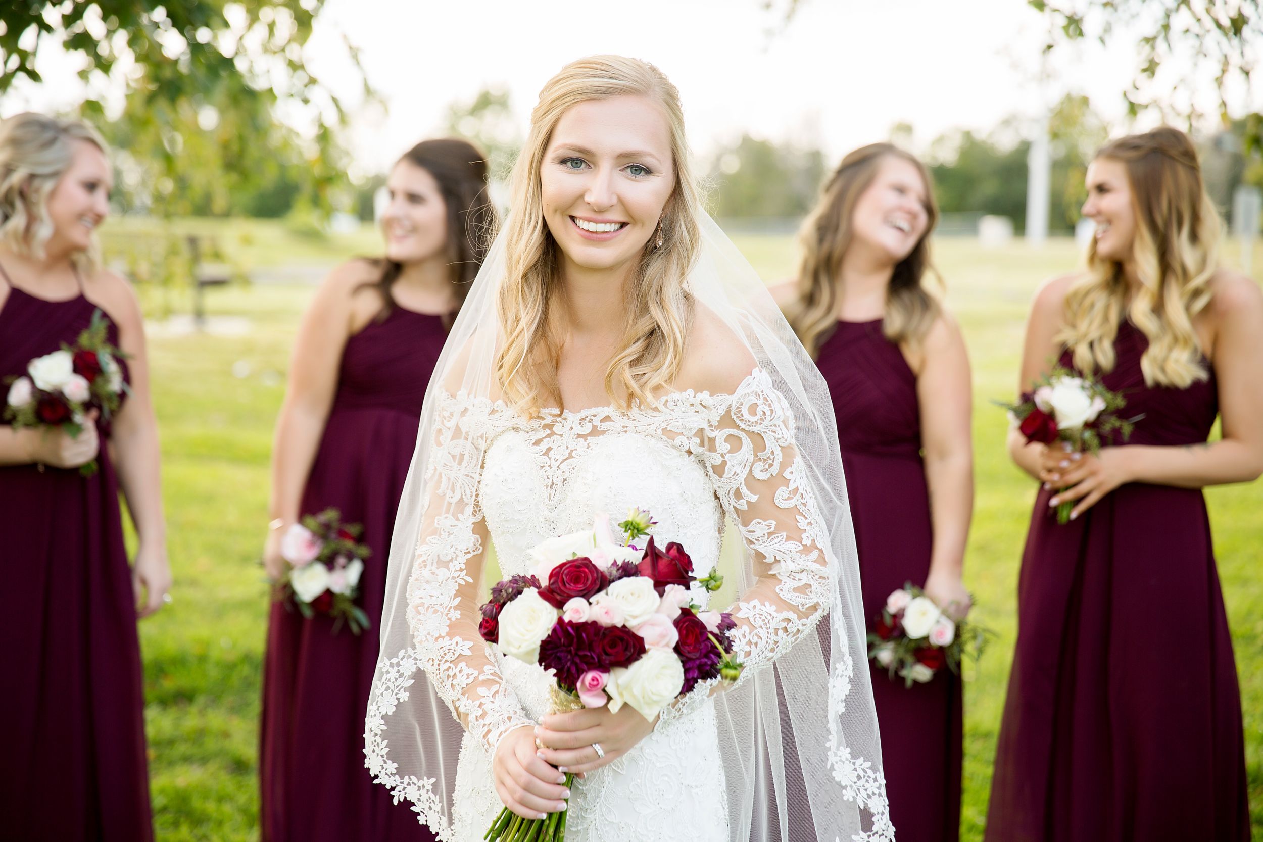 Wedding party poses outdoors with burgundy bridesmaid dresses and white floral bouquets.