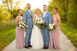 Wedding party in light blue suits and blush pink dresses poses together on a sunlit path.