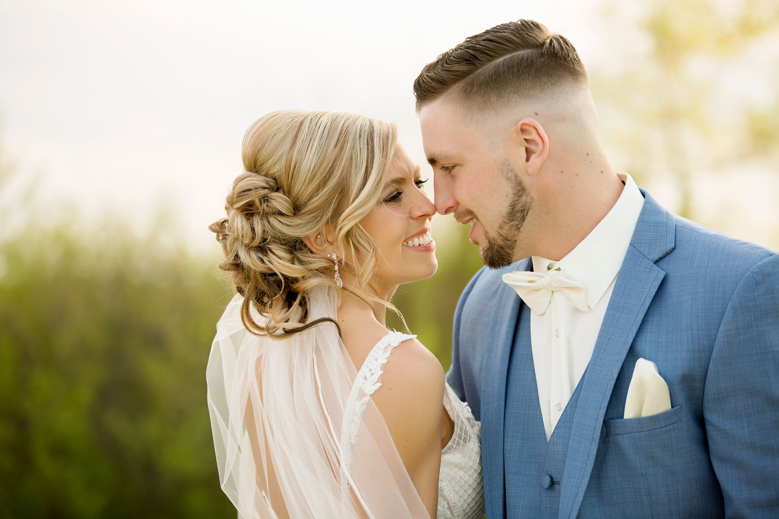 Intimate wedding portrait of couple in formal attire against natural backdrop at sunset.