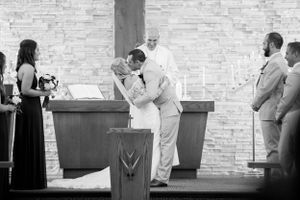 Black and white photograph of intimate wedding ceremony moment in modern church setting.