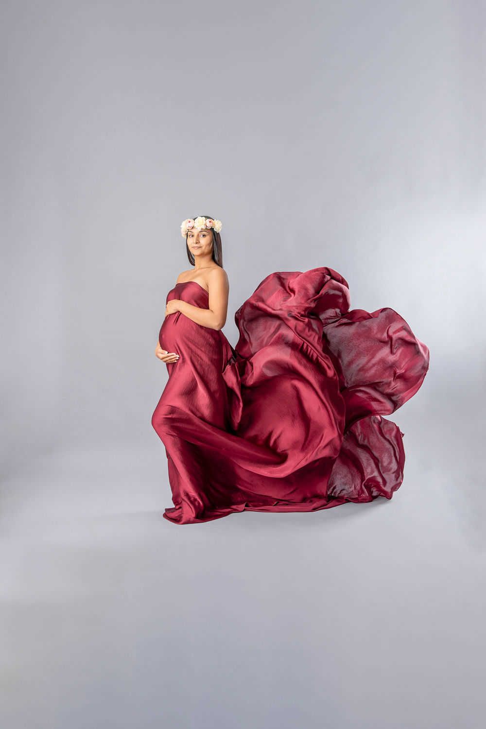Un portrait de maternité mettant en vedette un tissu de soie bordeaux fluide ondulant de manière spectaculaire autour d'une future maman