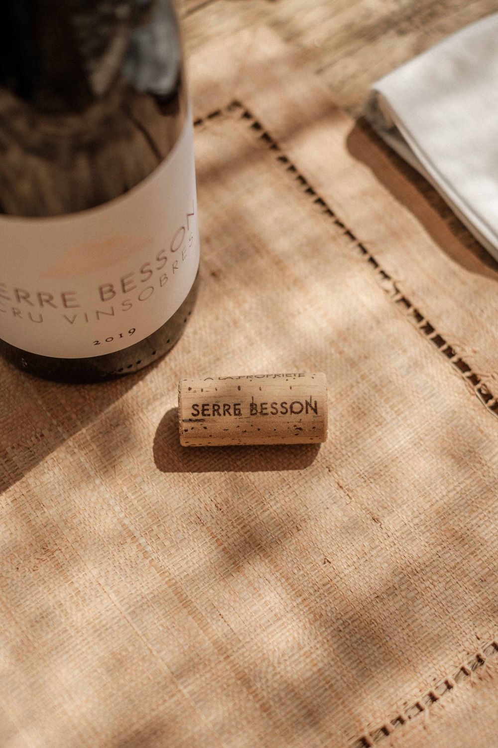 A wine bottle and cork from Serre Besson winery on a textured linen tablecloth.