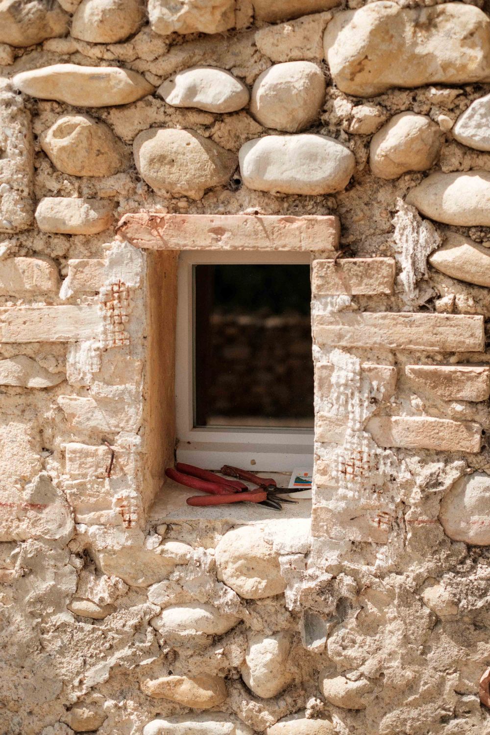 A small window in a rustic stone wall showing glimpses of an interior space.