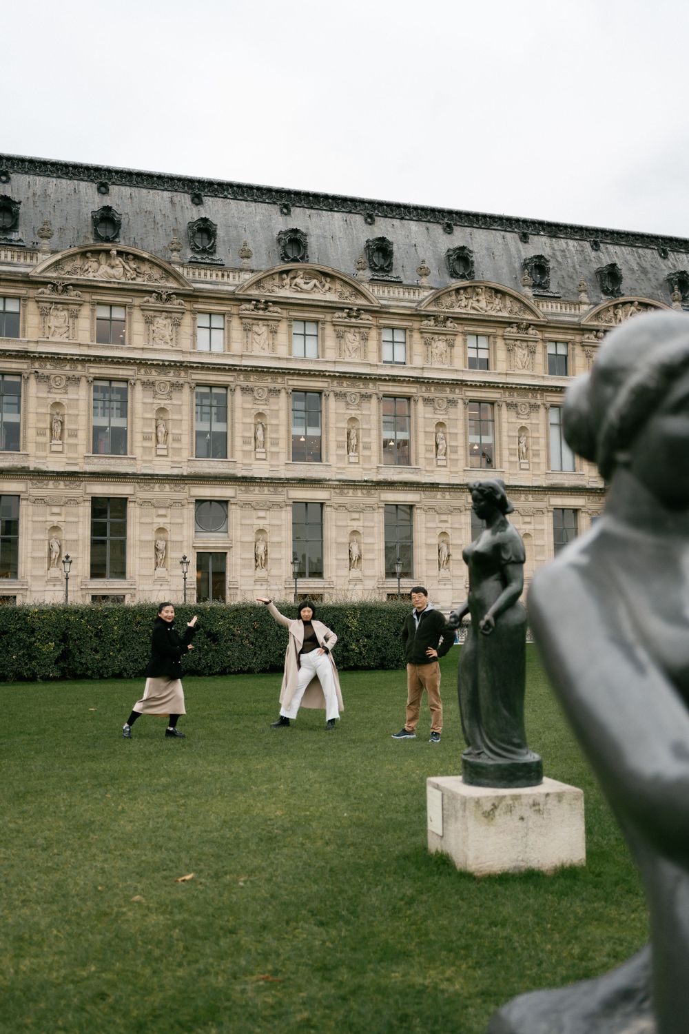 Tourists explore the gardens of a grand French palace with ornate classical architecture and decorative statues.