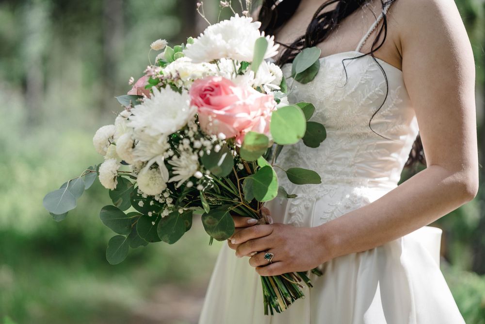 A bridal bouquet of pink and white flowers with eucalyptus greenery is held against a white lace dress.