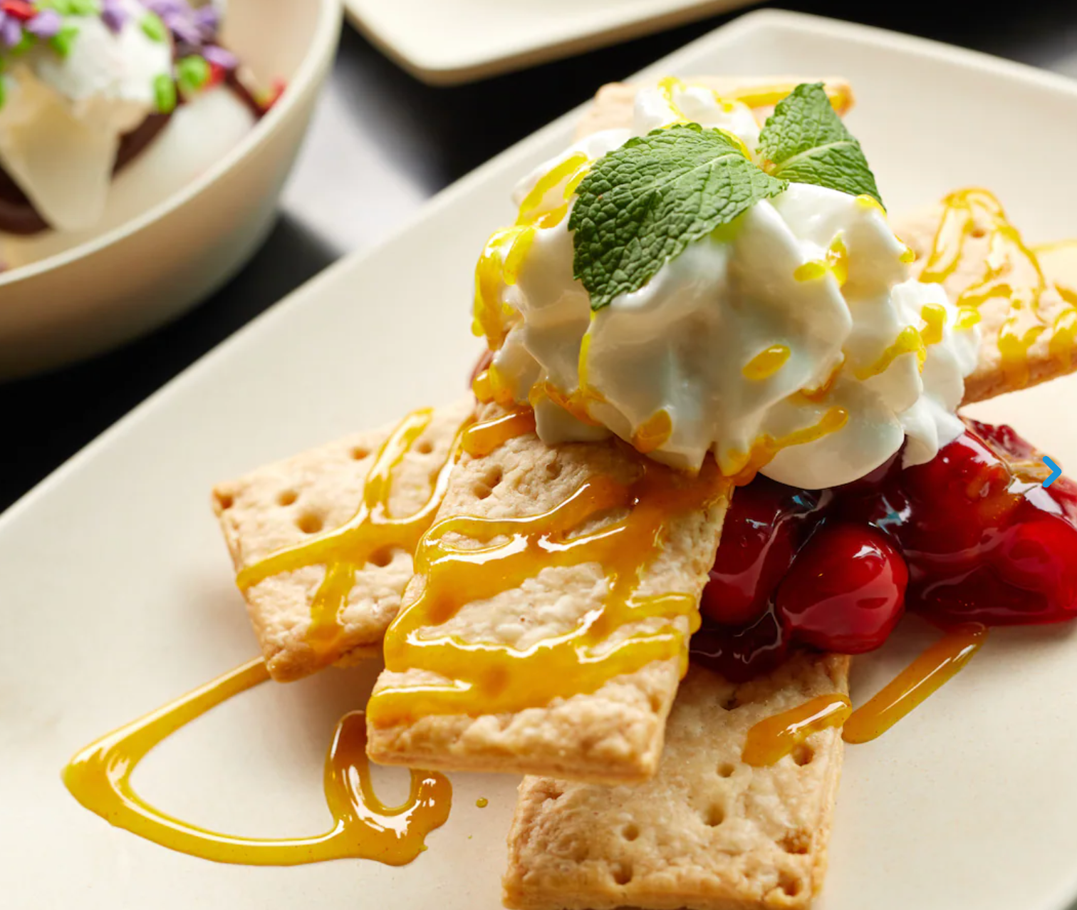 Delicate pastry topped with whipped cream, yellow sauce, and mint leaf on white plate.