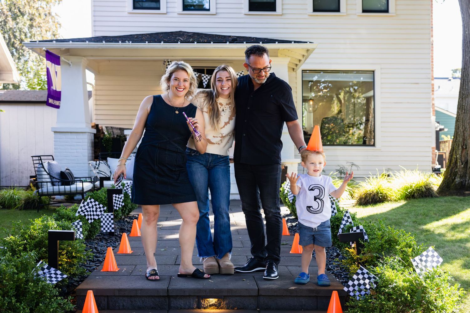 A group stands on a decorated porch with Halloween decorations and orange traffic cones creating a festive outdoor scene.