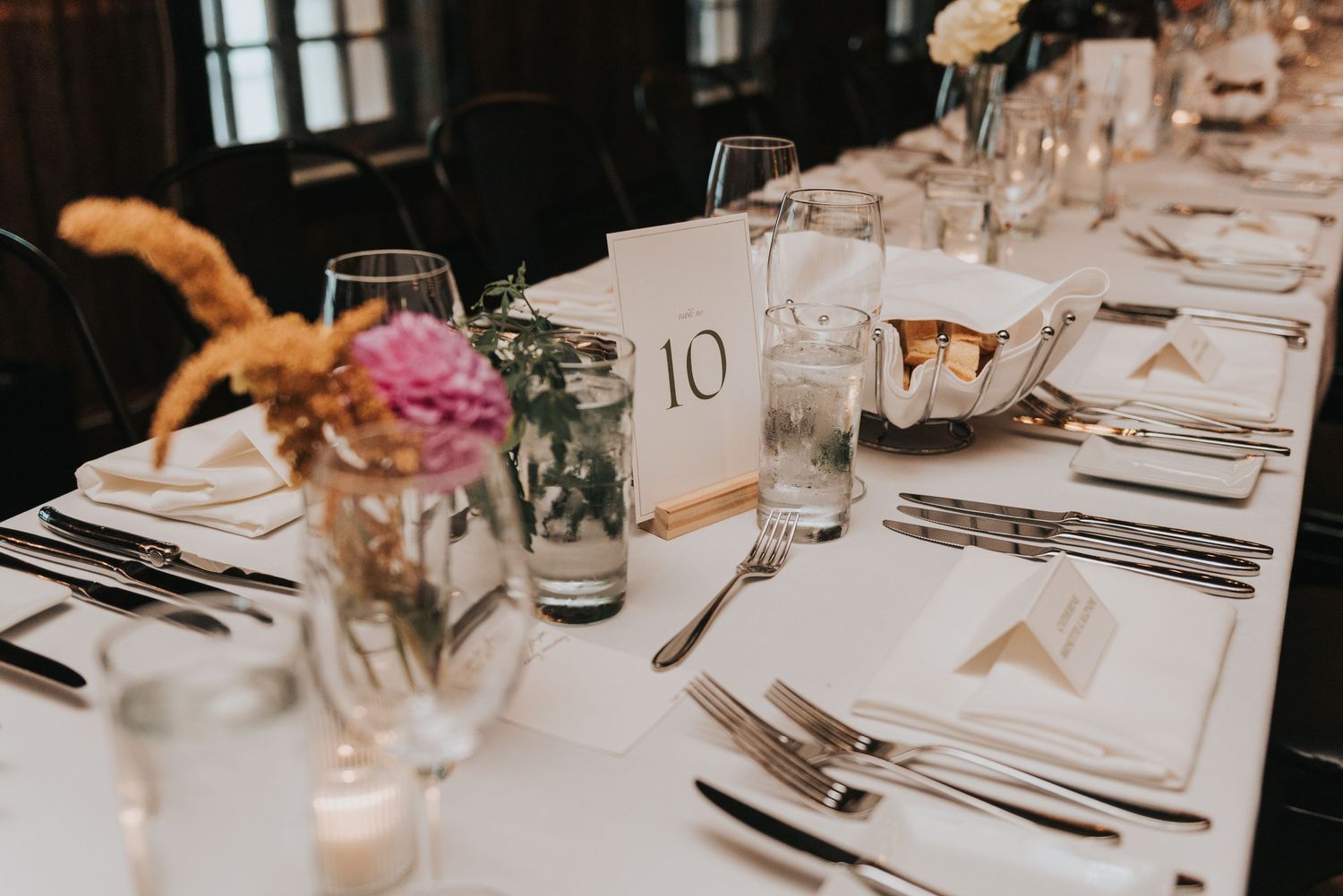Elegant table setting with white linens, table number 10, and pink floral centerpiece at wedding reception.