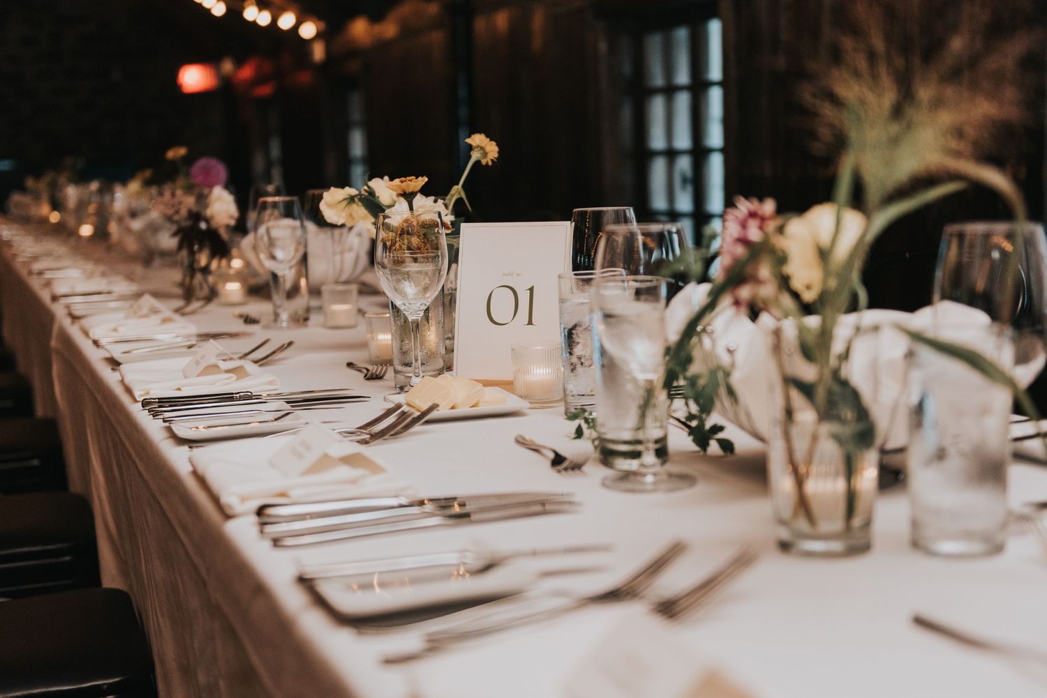 Elegant wedding reception table setting with table number, glassware, and floral arrangements on white linens.
