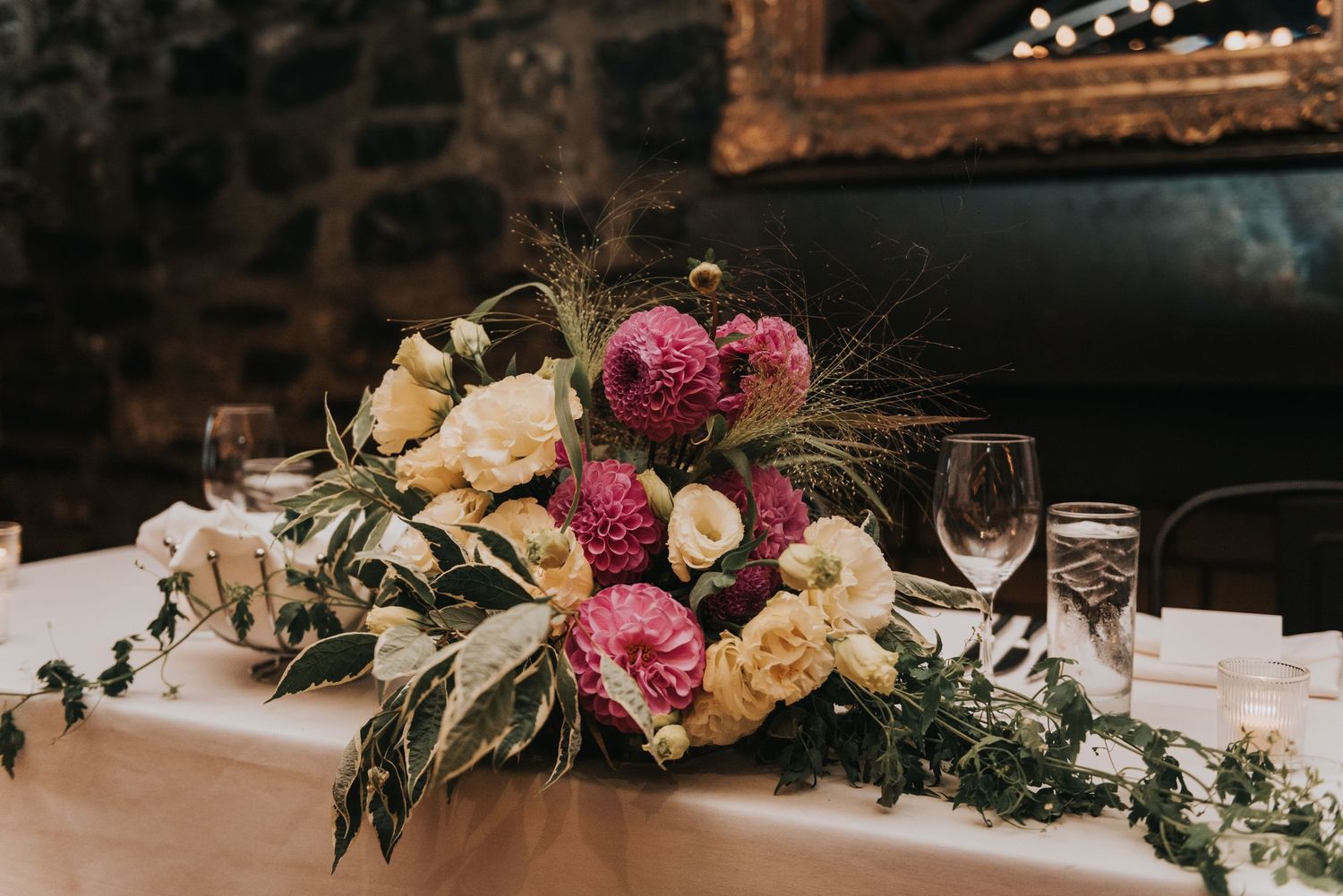 Elegant floral centerpiece with pink and cream peonies, eucalyptus leaves, and wine glasses on a rustic wooden table.