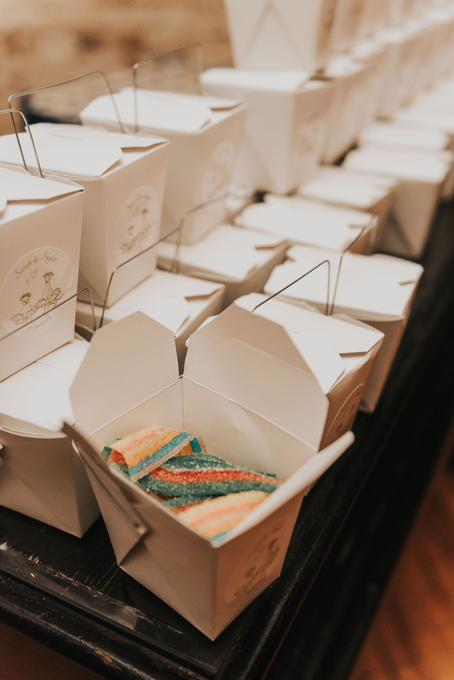 White takeout boxes containing colorful gummy worm candies arranged on a dark surface.