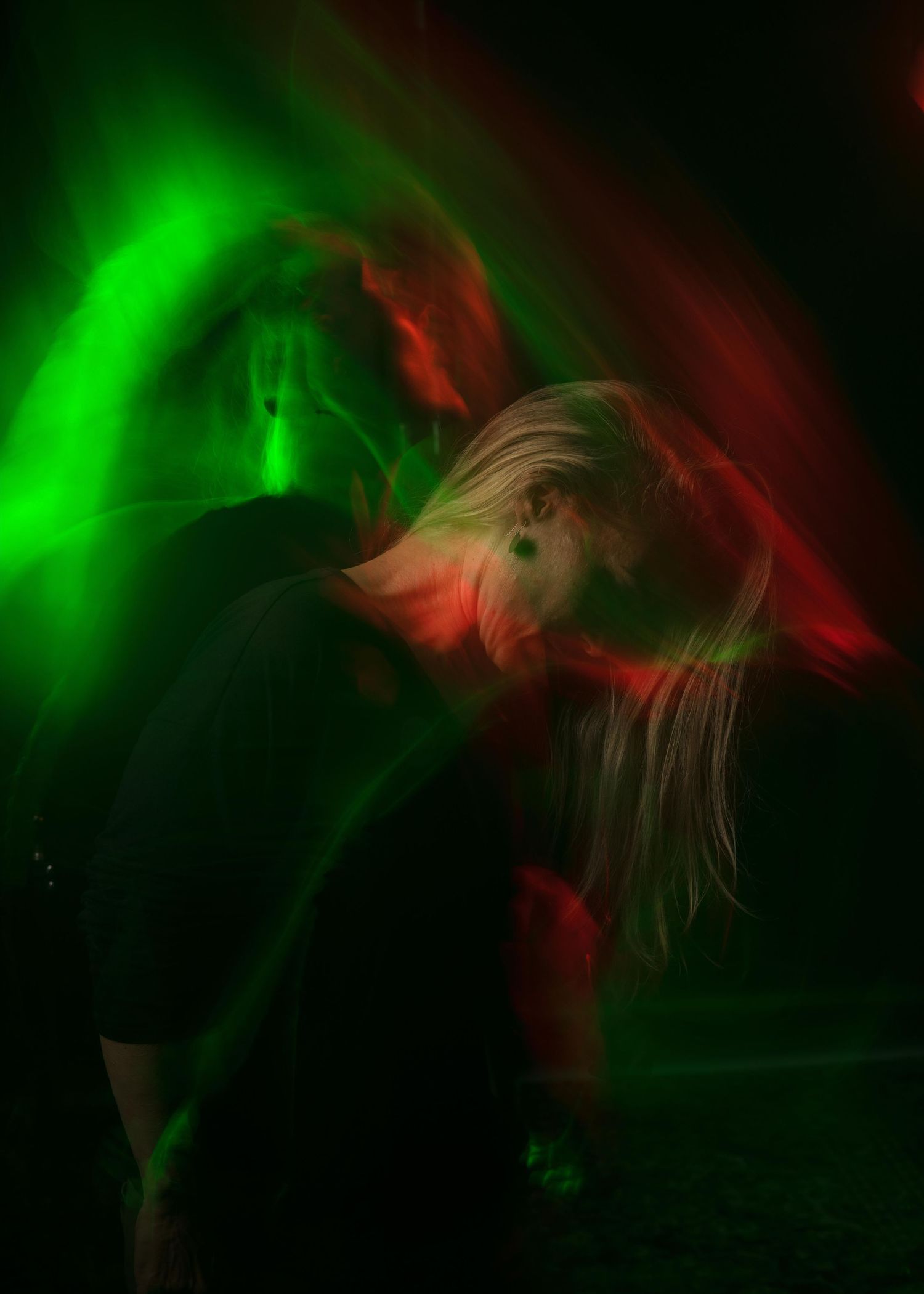 Artistic portrait with dramatic red and green lighting effects creating a moody dance-like movement in darkness.