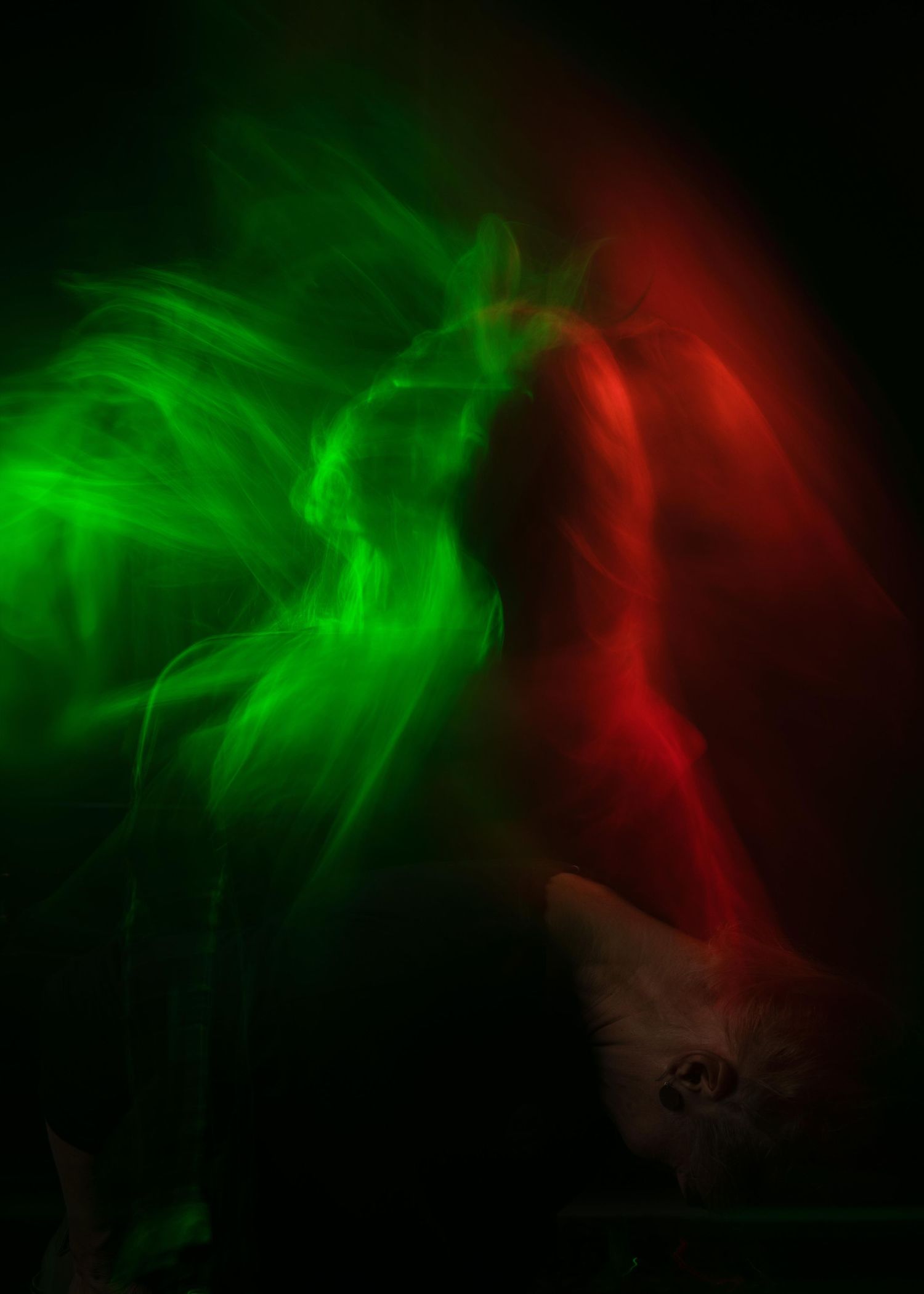Abstract swirling smoke effect in vibrant green and red colours against dark background creates ethereal atmospheric art.