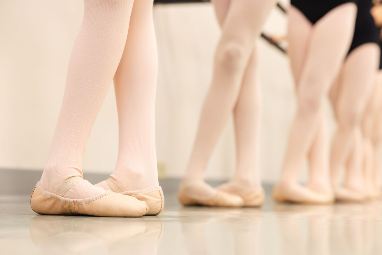 Ballet dancers' feet lined up at the barre wearing pink ballet slippers during dance class.