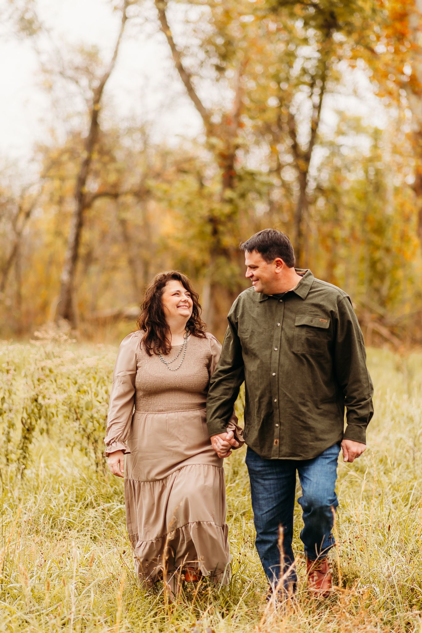 Couple walking together through tall autumn grass at sunset.