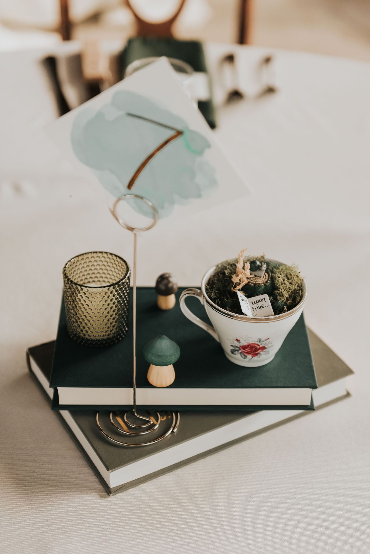 A vintage teacup with moss and decorative items arranged on stacked books with a glass votive holder.