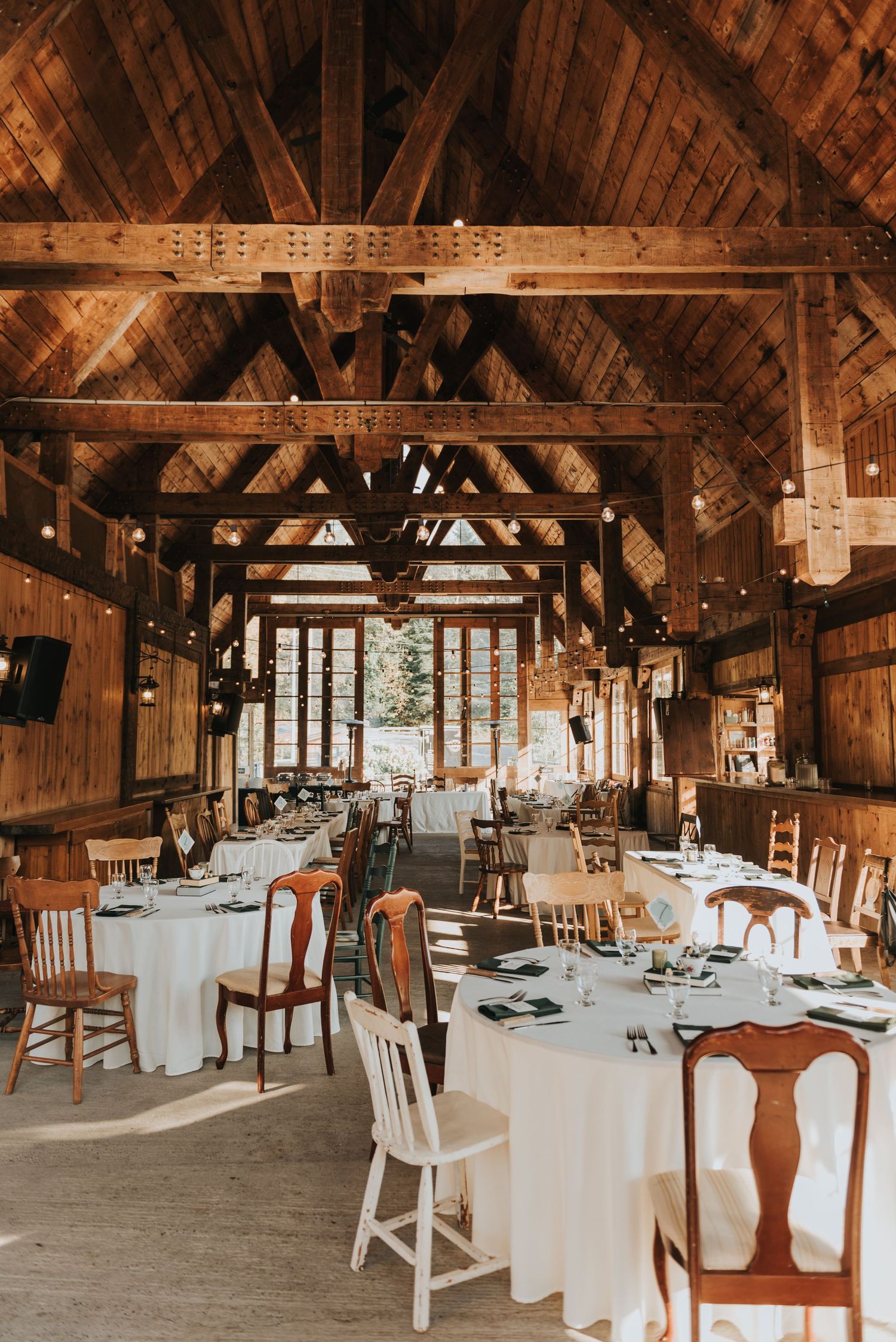 Rustic barn wedding venue with exposed wooden beams, white tablecloths and vintage wooden chairs set for reception.
