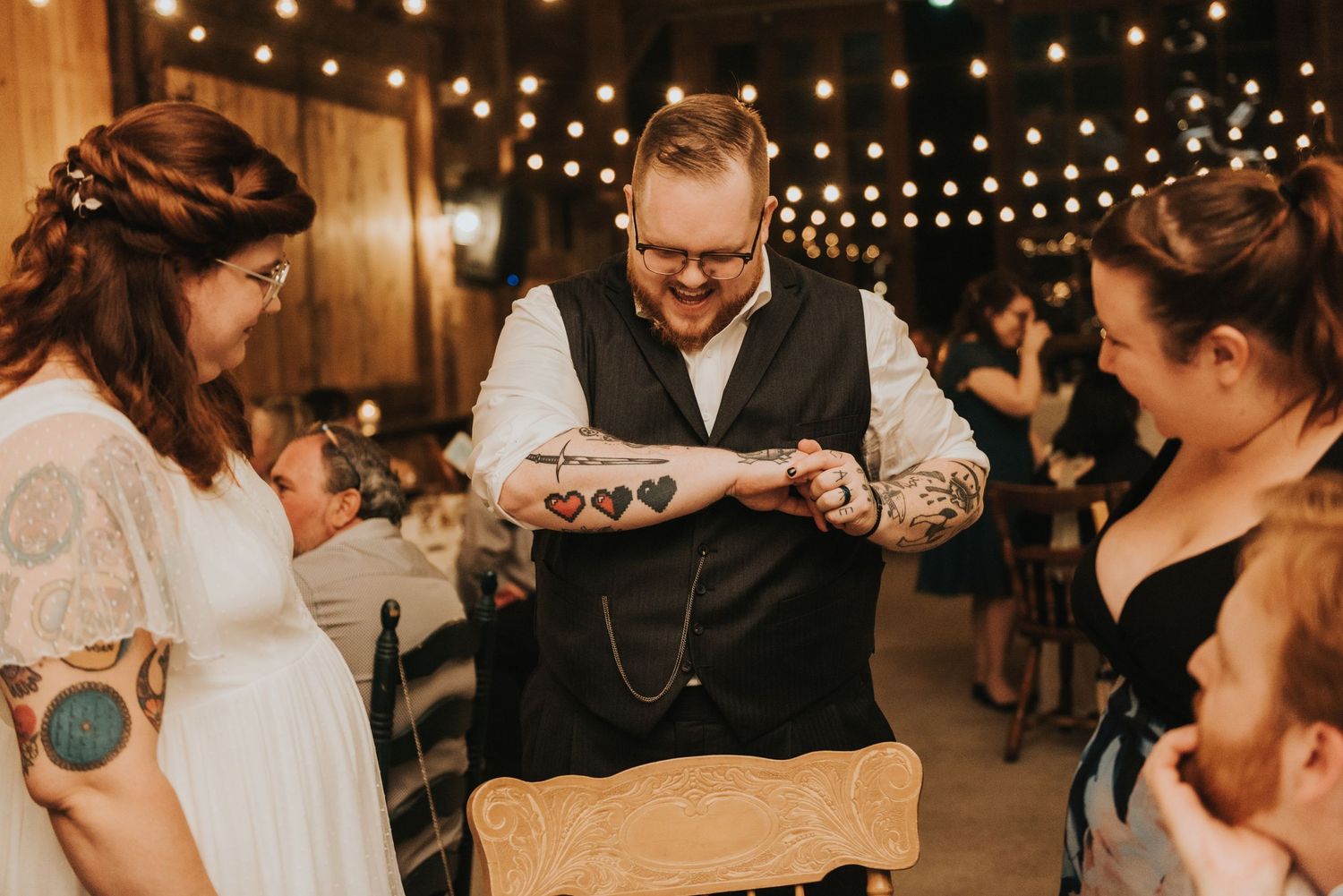A warmly lit rustic barn wedding reception with string lights overhead as guests gather around for a special moment.