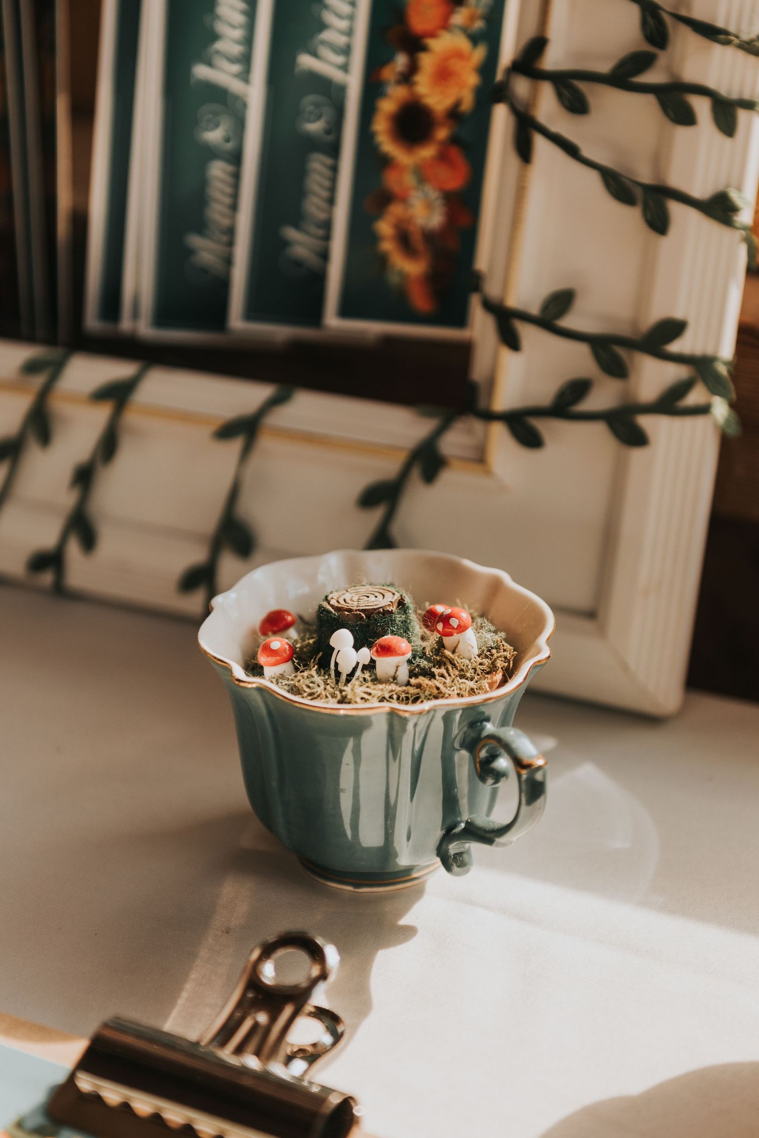 A teal ceramic mug filled with granola, topped with berries and nuts sits on a white surface near books and decorative vines.