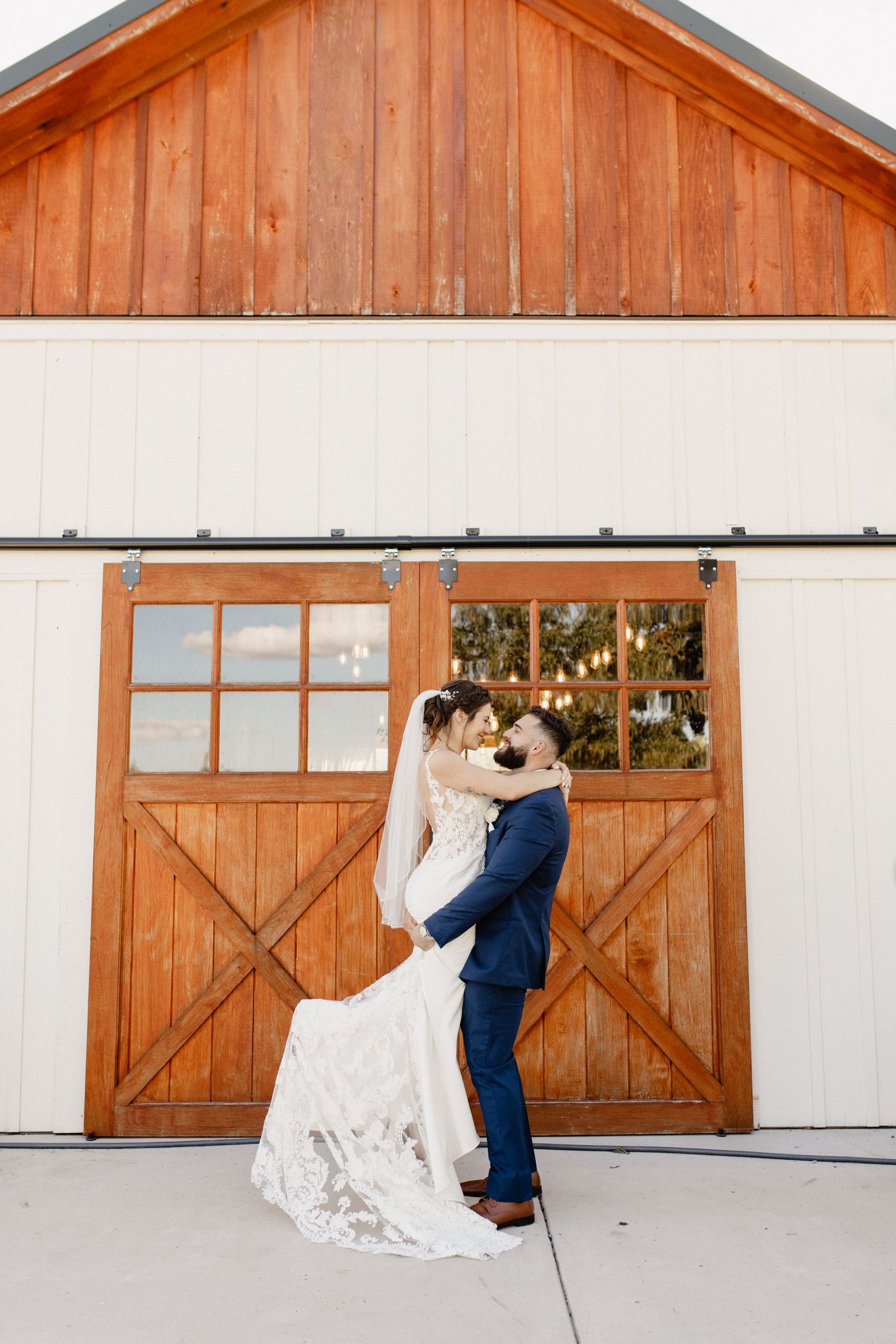 A romantic wedding couple embraces in front of a rustic barn with sliding wooden doors.