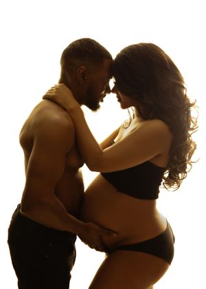 A silhouetted couple in an intimate embrace sharing a tender moment during a maternity photo in Vanessa Charlotte Photography luxury studio