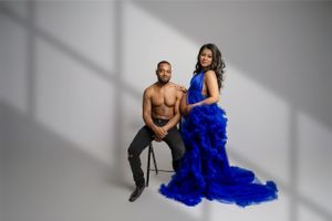 Two people pose in luxury studio setting against white backdrop, with one wearing a dramatic royal blue gown. Vanessa Charlotte Photography