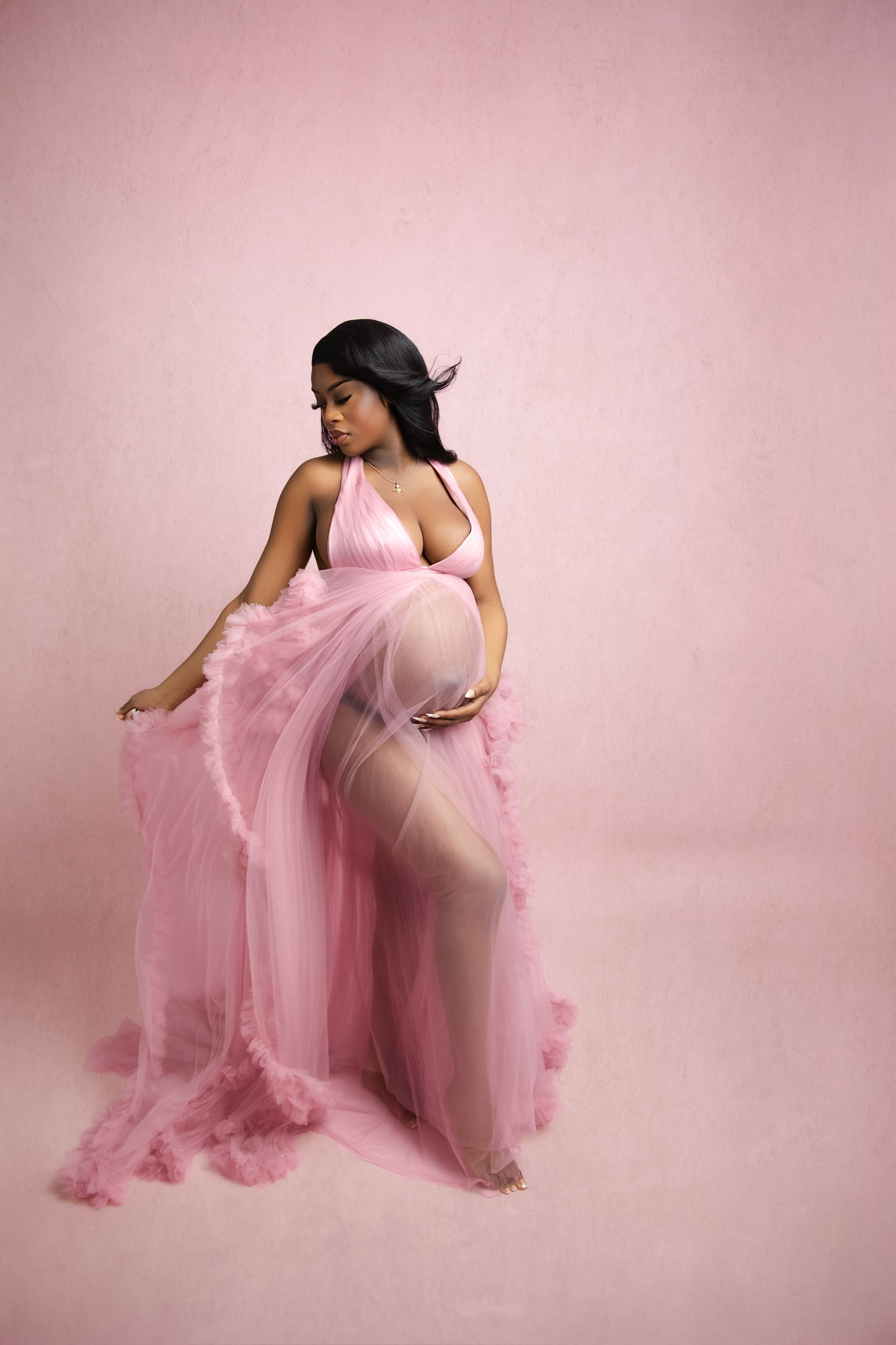 A glamour photo featuring a flowing pink tulle gown against a soft pink backdrop in a dreamy studio setting.