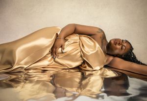 Person lying gracefully in luxurious gold satin gown with reflective surface creating elegant mirrored effect.