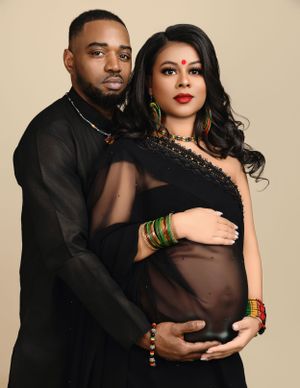 A maternity photo featuring a couple in black attire posing against a neutral background.