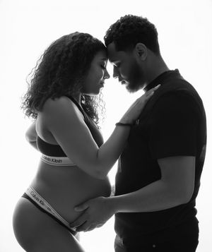 A tender black and white maternity photo of a couple in Calvin Klein intimates embracing in silhouette against a white backdrop.
