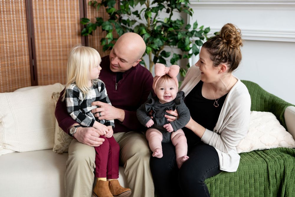 Cheerful family with two young daughters sitting together on white couch in living room.