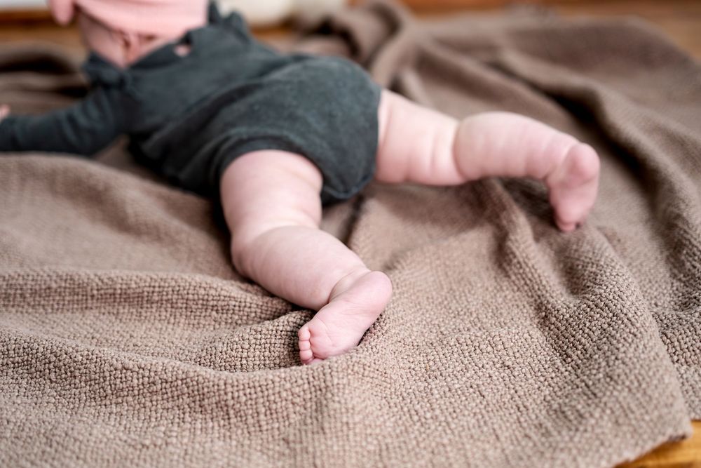 Close-up of a baby's tiny feet and legs resting on a soft brown textured blanket.