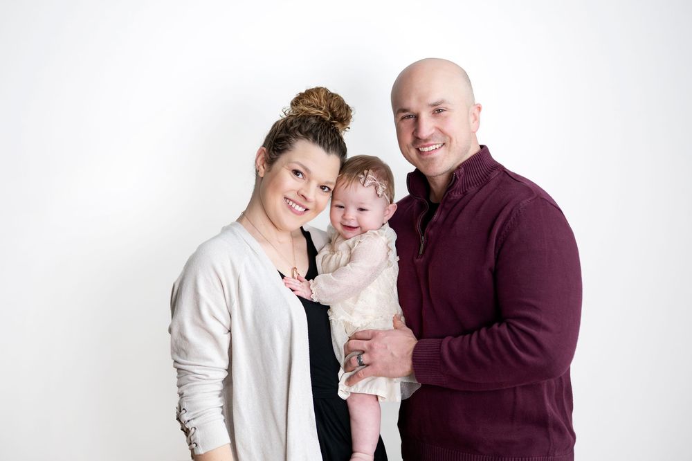 Smiling couple posing with their baby girl in a bright studio family portrait session.