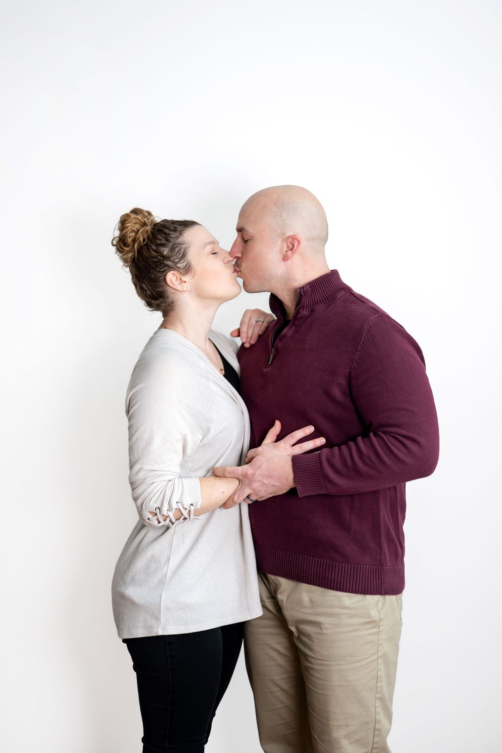 Romantic couple sharing a kiss in an intimate studio portrait against a white background.