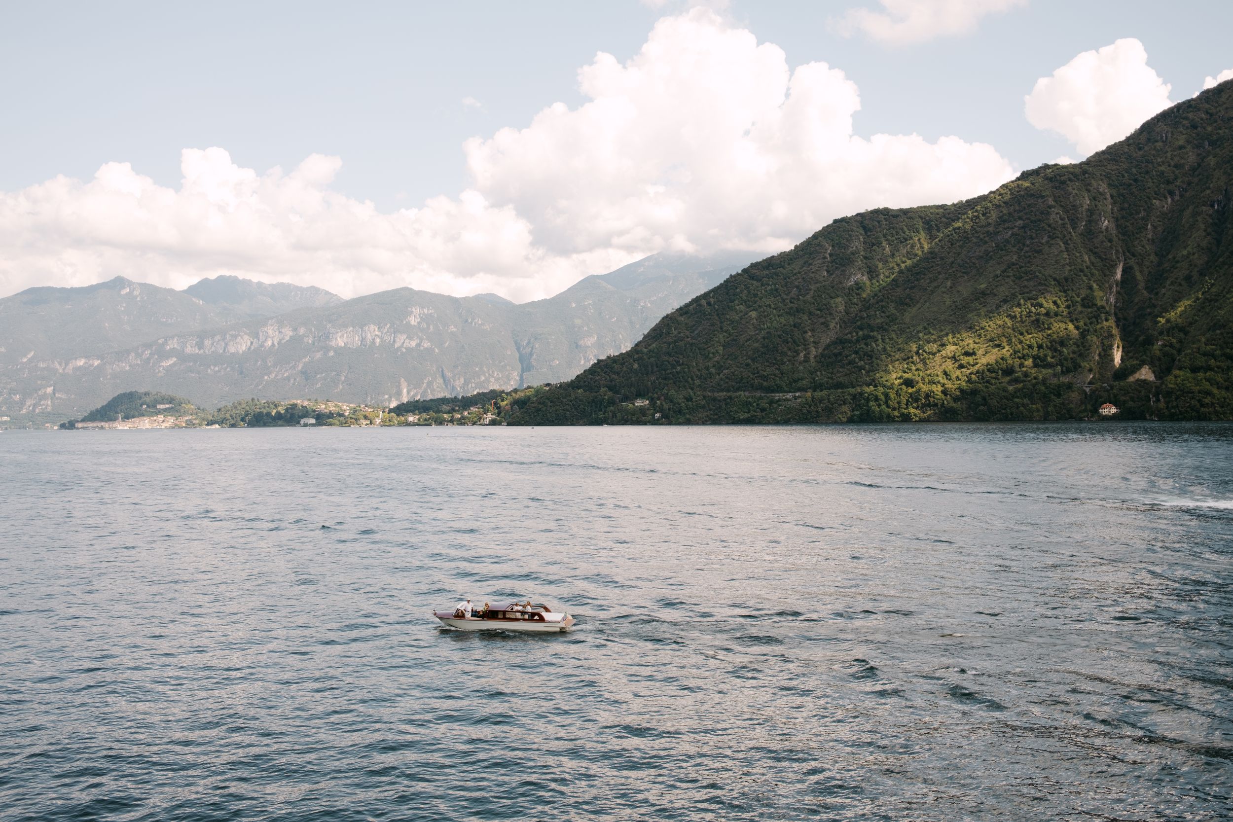 A scenic panoramic view of a lake surrounded by mountains with a boat sailing across calm waters on a cloudy day.