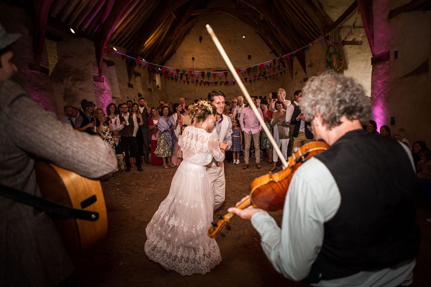 Wedding guests dance and celebrate on a dimly lit dance floor during an evening reception celebration.