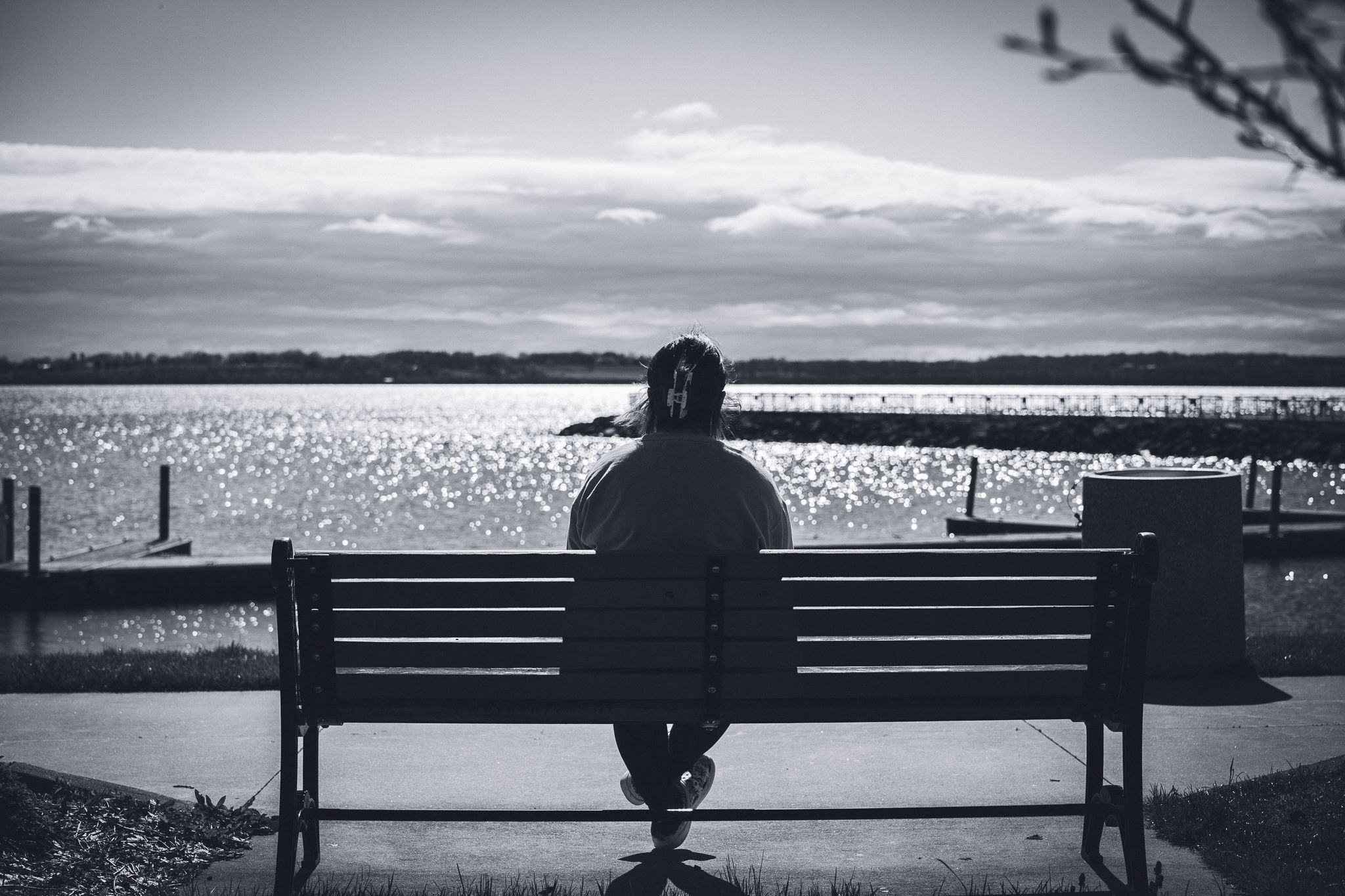 Silhouette of person sitting alone on bench overlooking water during cloudy day.
