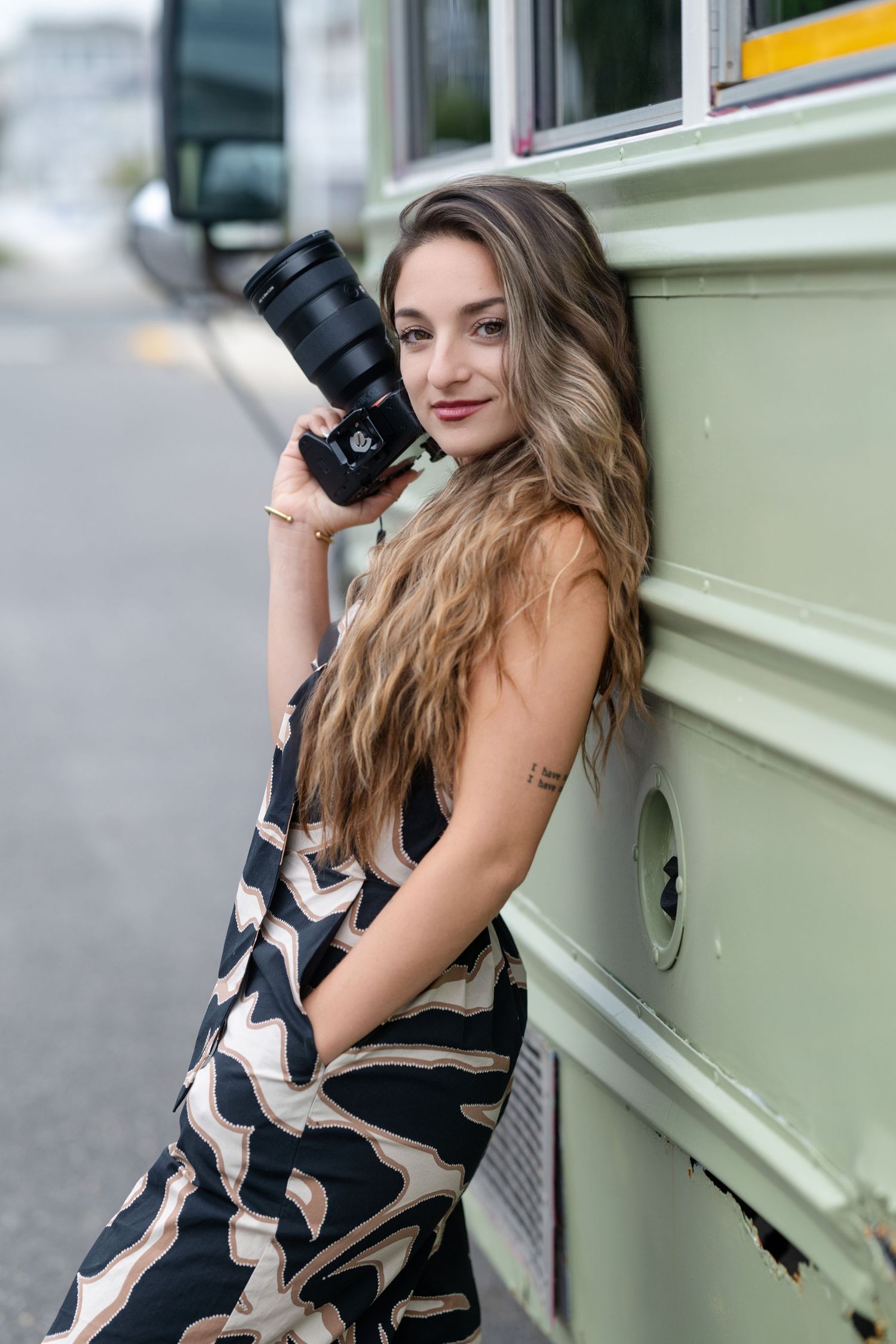Photographer with camera posing against vintage bus exterior for creative portraits.