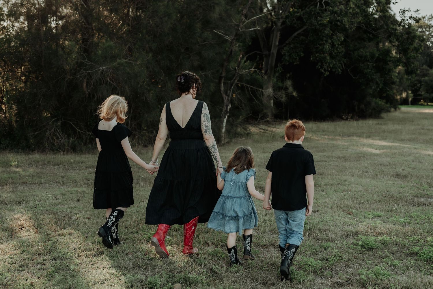 A group of four people walking together through a gladstone grassy field at dusk, holding hands in a line.