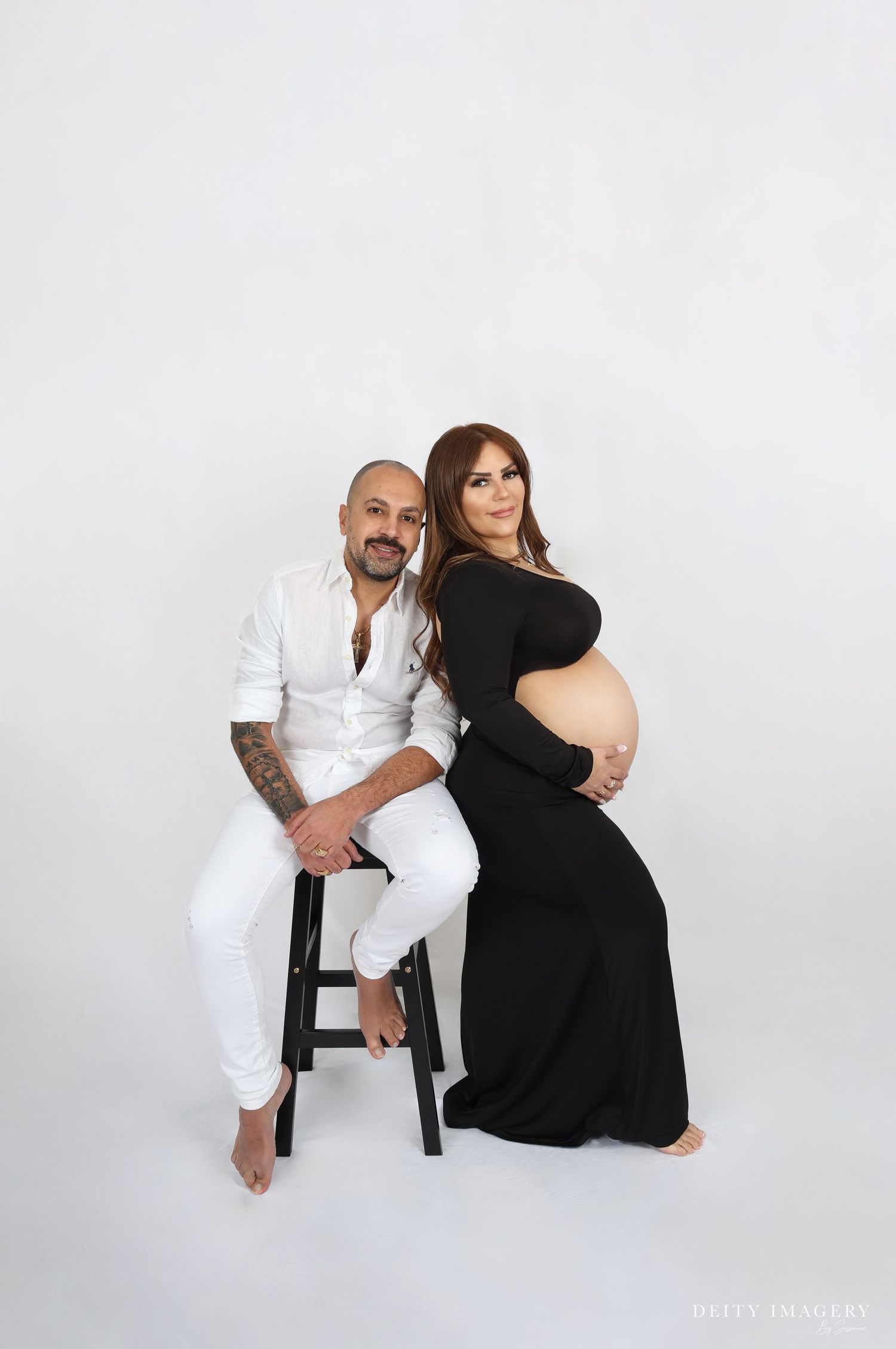A couple poses together in a studio setting against a white backdrop wearing contrasting black and white outfits.