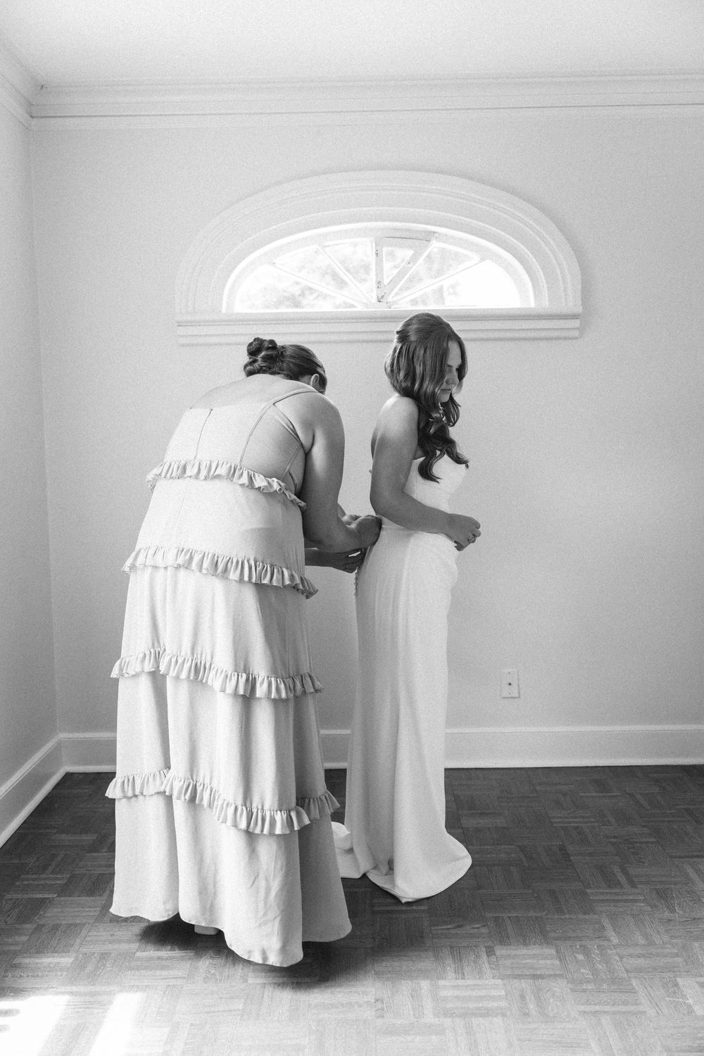 Black and white photo series showing figures in white dresses bending down in an empty room with hardwood floors.