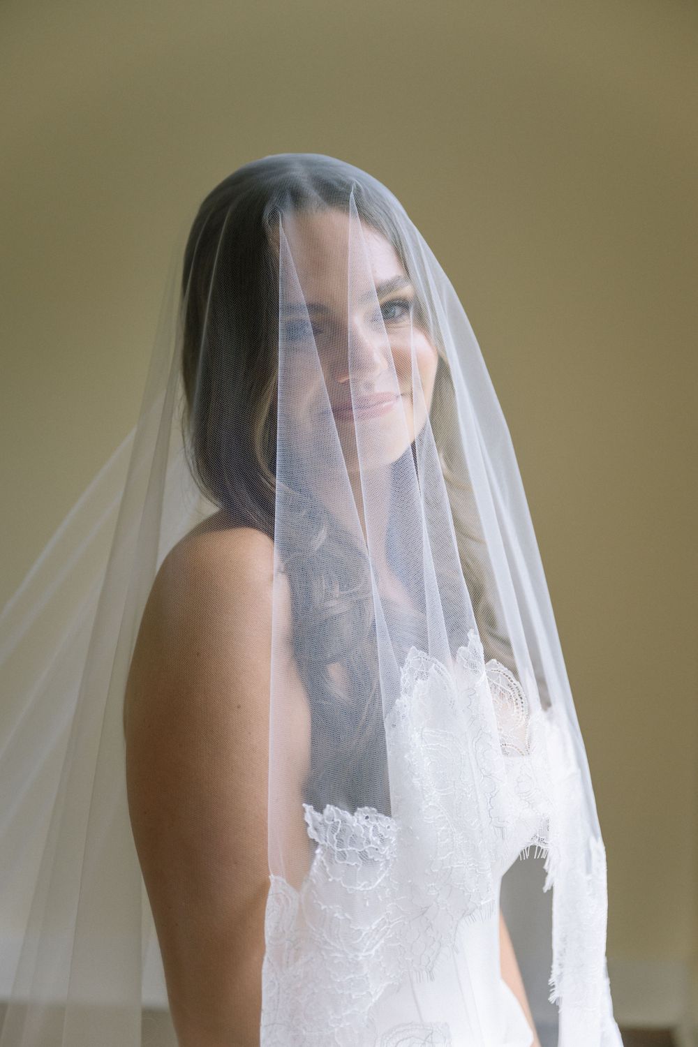 A delicate bridal portrait showing a soft smile through a sheer white veil.