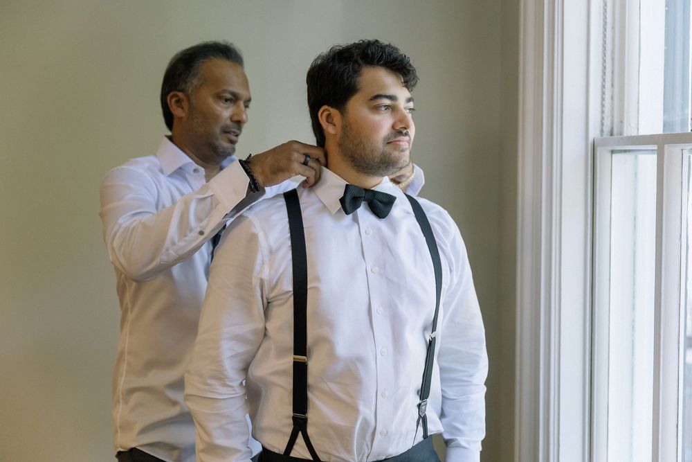 Groomsmen adjust their bow ties and suspenders while getting ready.