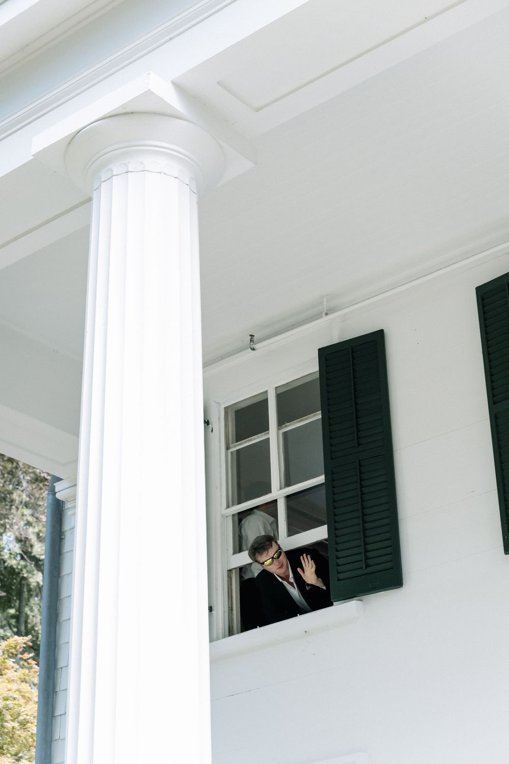 White colonial style house exterior with dark shutters and elegant columns in daylight.