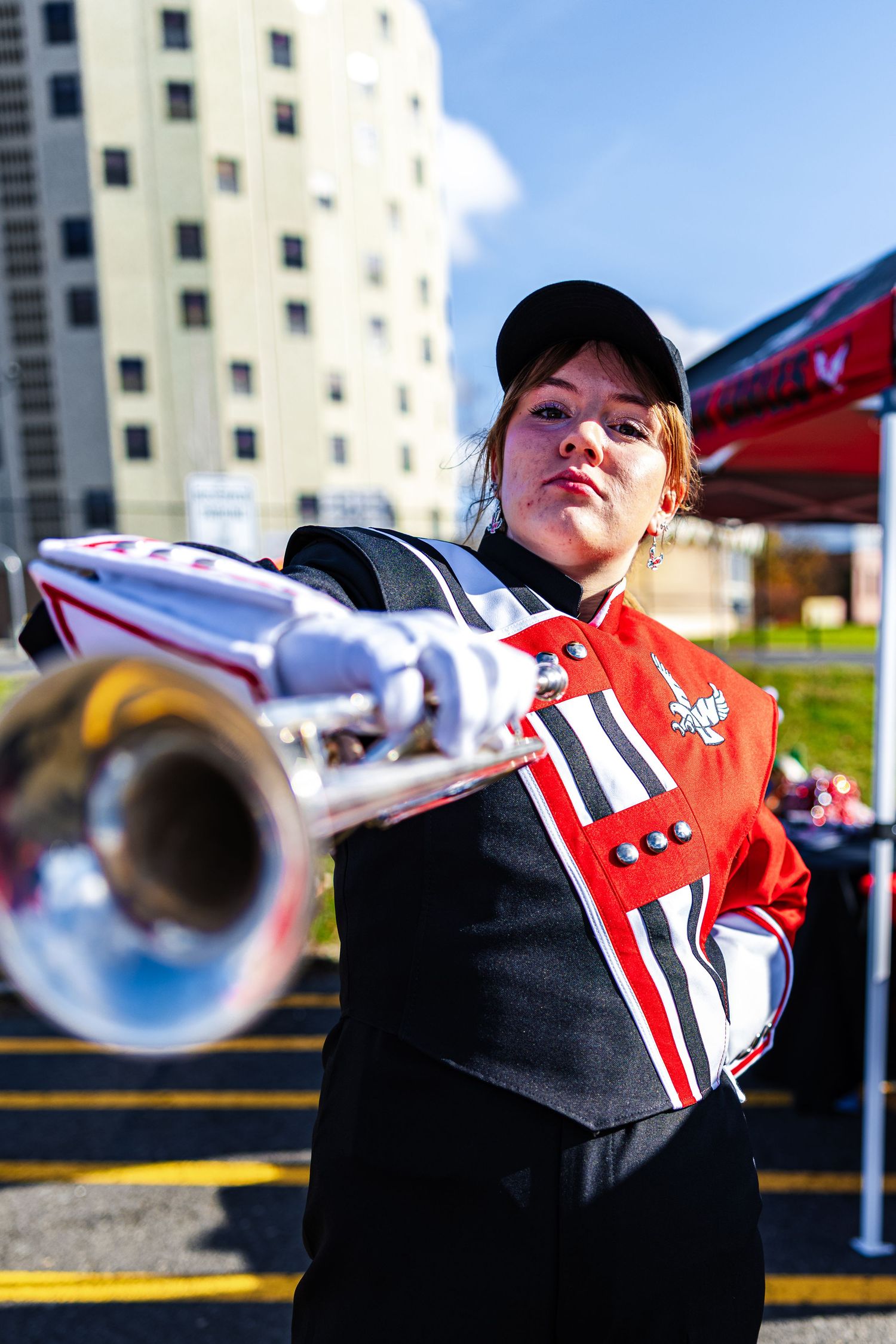 Four sequential photos show a trumpet player in red and black uniform performing during an outdoor event.