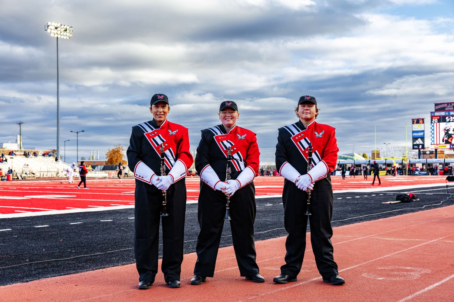 A panoramic sequence of track and field athletes sitting on a red running track under cloudy skies.
