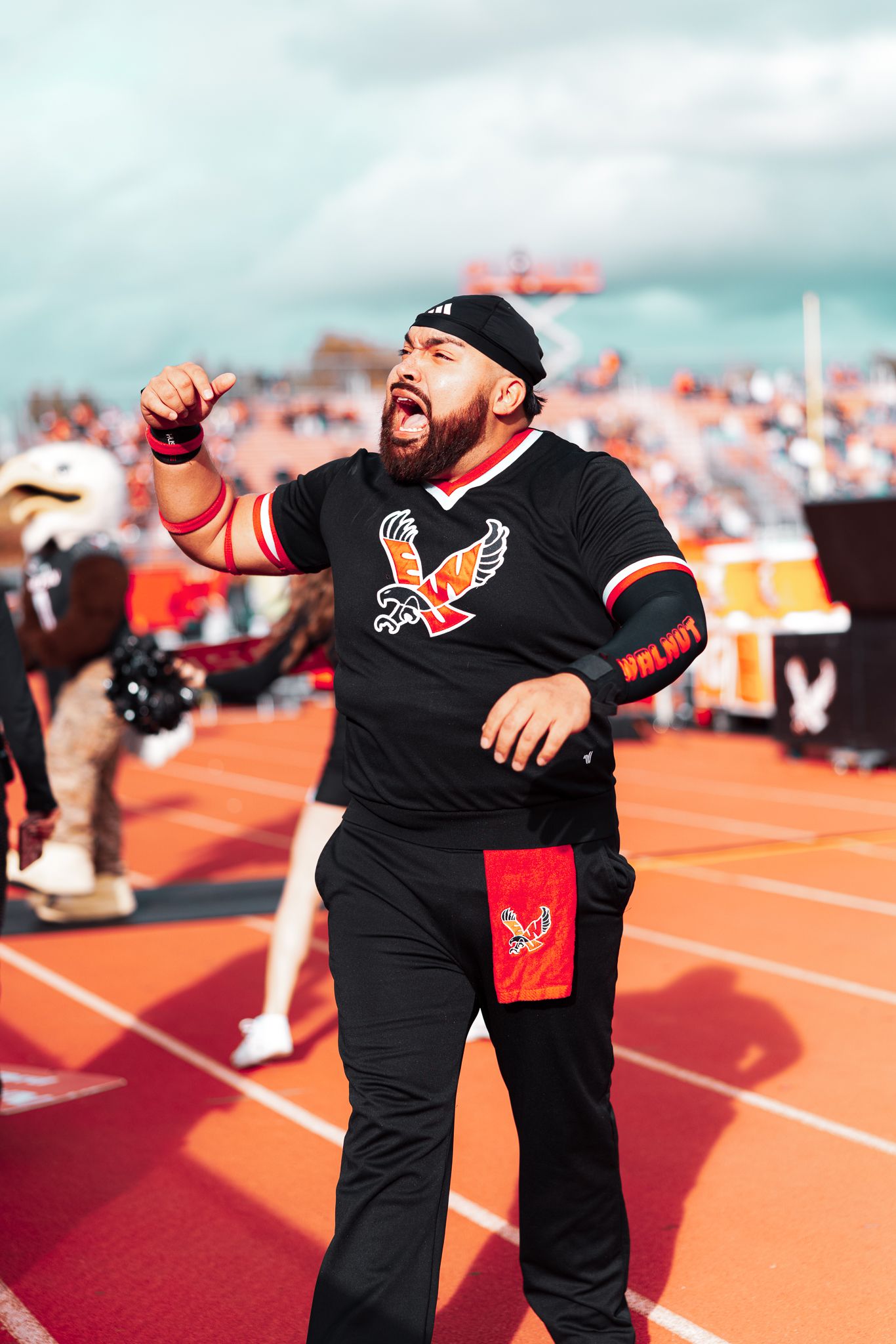 A person in black clothing performs an energetic dance routine on an orange running track at a stadium.