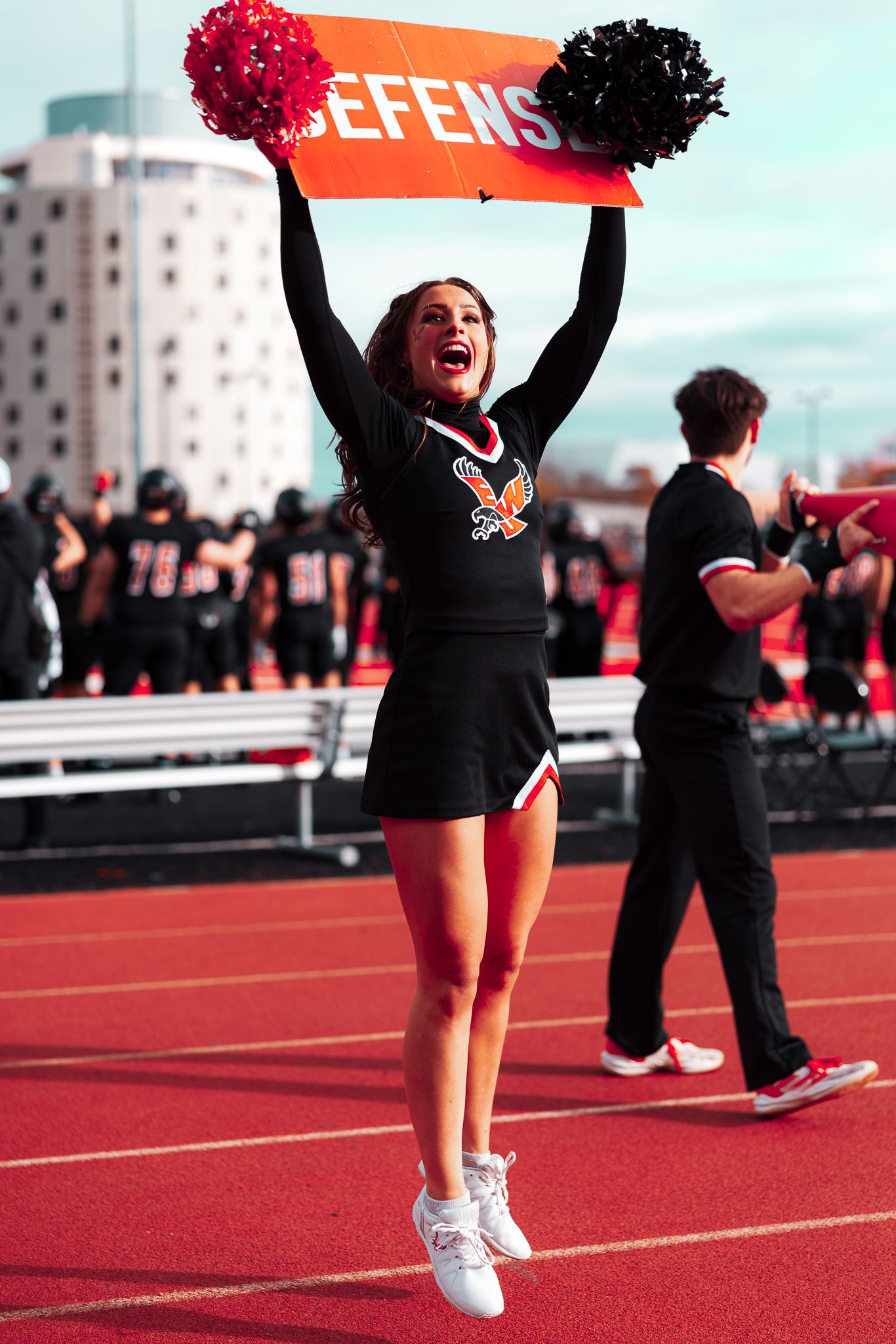Cheerleaders in black uniforms perform synchronized routines on a bright red athletic field during a sports event.