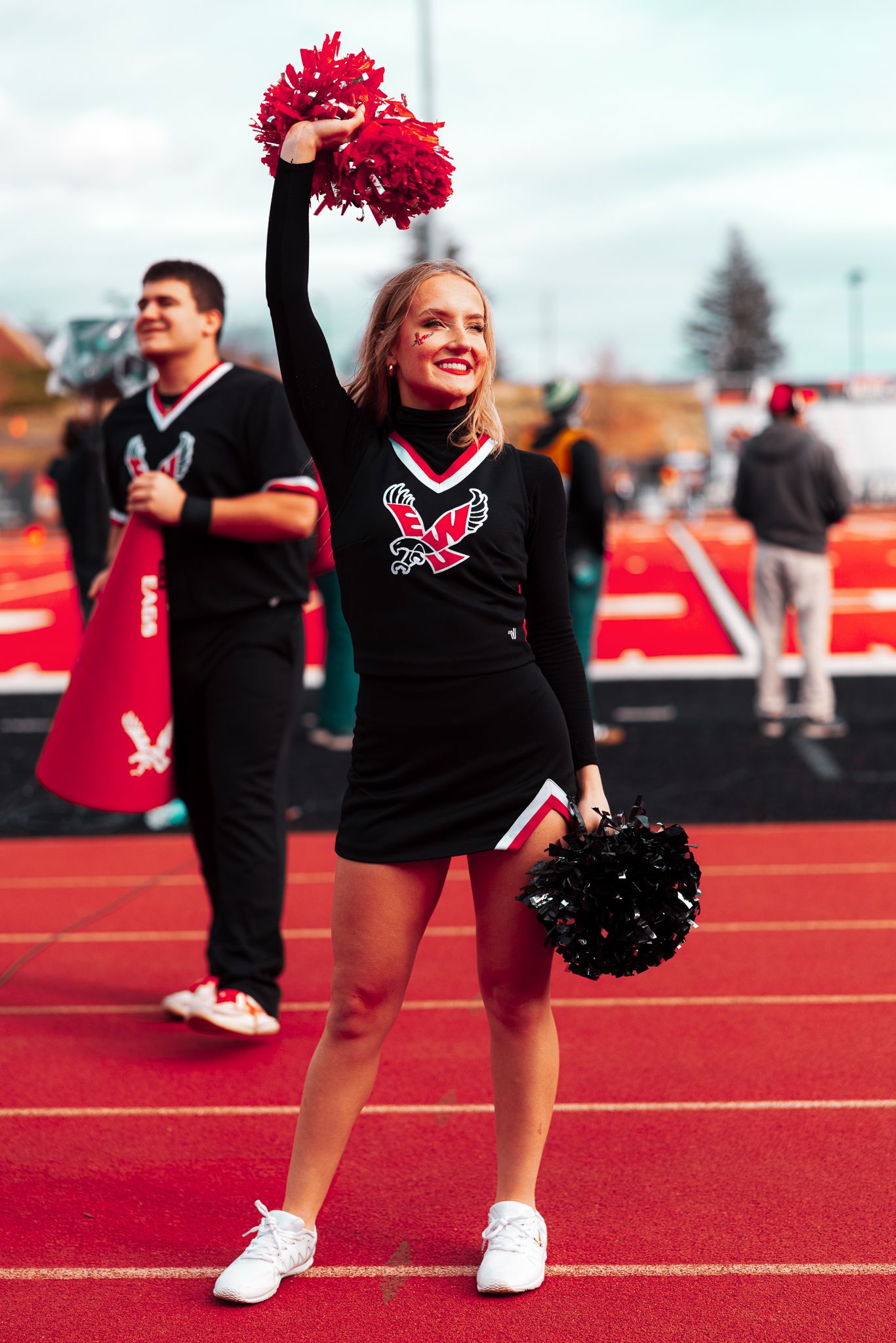 Cheerleaders in red and black uniforms performing on a red running track at an outdoor sports event.