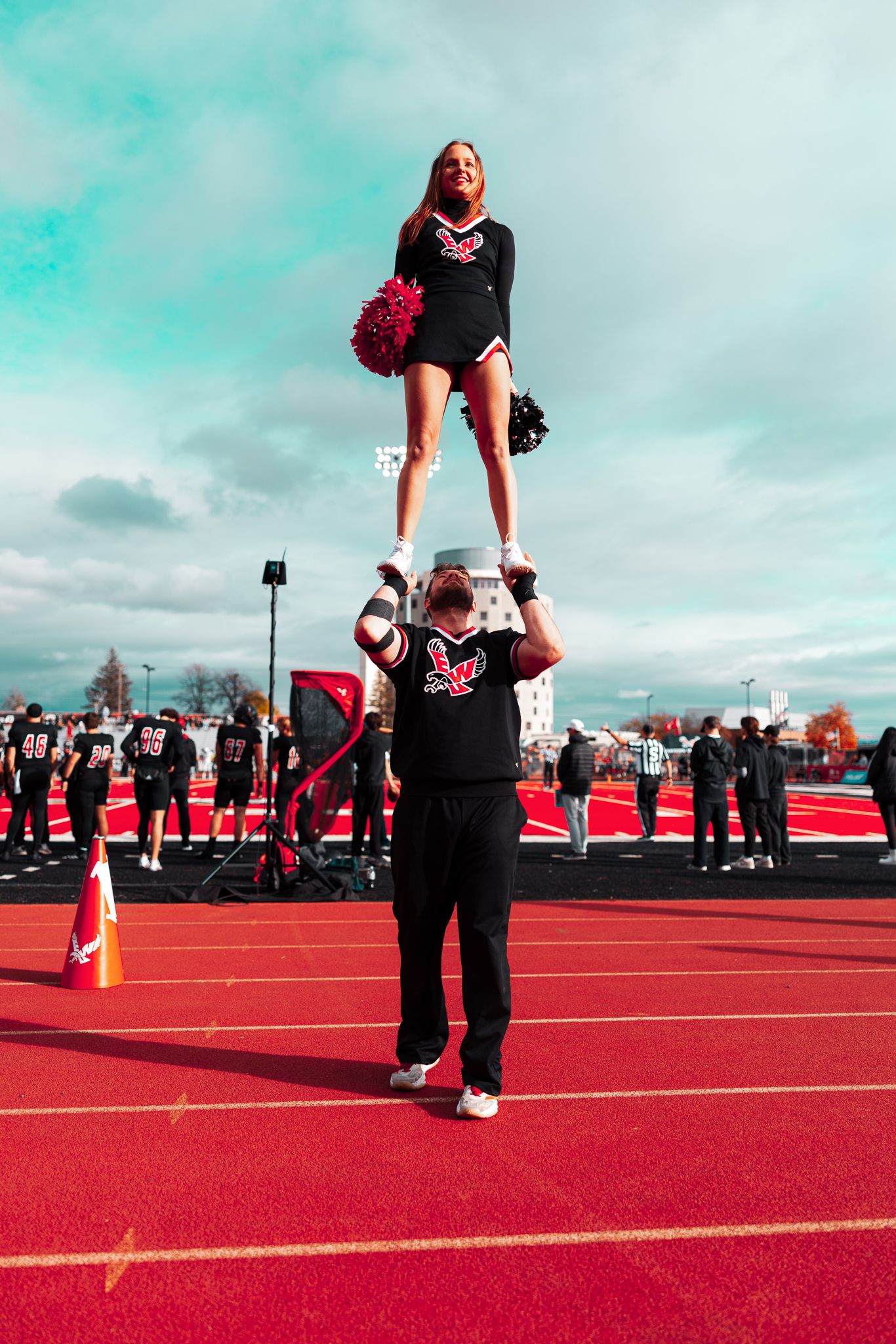 A sequence of cheerleading practice stunts being performed on a bright red athletic track under a turquoise sky.
